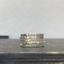 Load image into Gallery viewer, Stack of silver rings on a dark wooden surface with a light gray background