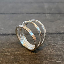 Load image into Gallery viewer, A triple silver ring with a polished finish, displayed on a wooden surface.