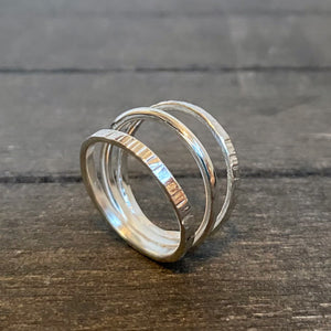 A triple silver ring with a polished finish, displayed on a wooden surface.