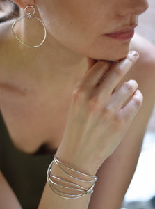 picture of a women wearing three silver dangle wave bracelets and silver wave earrings